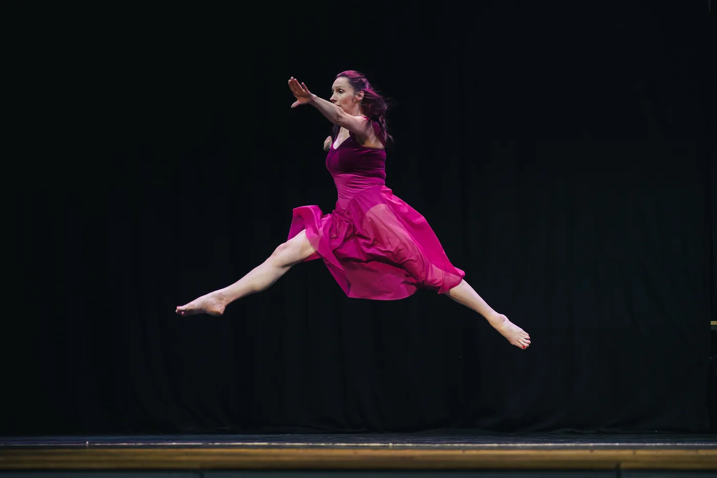 An ASD Dance performer soaring in a leap on stage